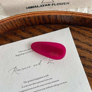 Detailed macro view of a rose red acetate teardrop hair clip with gold handmade lettering