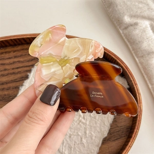 Elegant tortoiseshell acetate claw hair clip set on a wooden tray and white linen fabric
