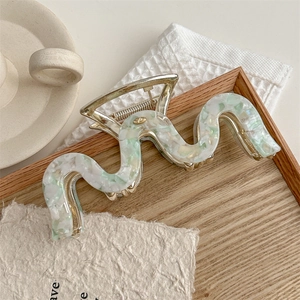 Detail view of large marble wave hair claw clip on wooden tray in cozy lifestyle setting