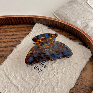 Detailed view of acetate hair claw clip with tortoise pattern and gold logo text