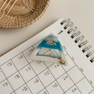 Detailed close-up of a blue and white ombré acetate triangle hair claw with gold logo