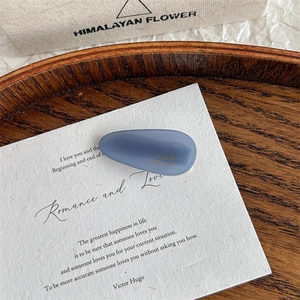 Detailed macro view of haze blue acetic acid waterdrop hair clip with gold logo text