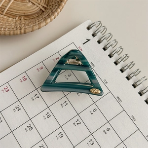 Detail view of triangular green marble acetate hair claw with a small gold logo