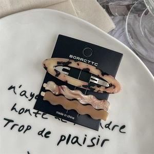 Gros plan de trois barrettes en acétate aux tons écaille et pastel sur une assiette blanche