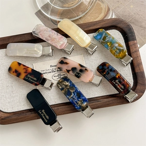Eight-piece set of elegant tortoise acetate hair clips with gold lettering on a wooden tray