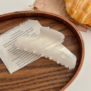 Macro detail of pearlescent cream acrylic hair claw clip on wooden tray with rustic decor