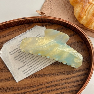 Detailed close-up of large marble acrylic hair claw clip with golden glitter on wood tray