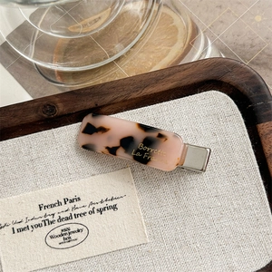 Detailed macro view of retro pink tortoiseshell acetate hair clip on a textured linen mat