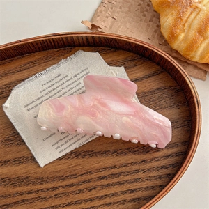 Detail of a large pink and white marble acetate hair claw clip on linen cloth