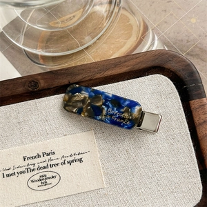 Close-up of retro marble pattern acetate hair clip with elegant gold lettering detail
