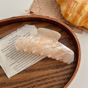 Close-up of marble pattern hair claw clip on wooden tray in a cozy lifestyle setting