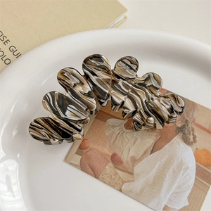 Macro detail of large acetate hair claw clip with marble texture on ceramic tray