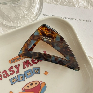 Close-up of tortoise shell acetate hair claw clip with blue marble pattern and gold logo