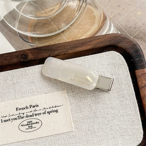 Detail of cream acetate hair clip with gold lettering on a rustic linen background