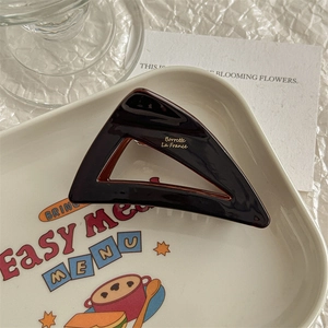 Close-up of a dark brown acetate triangle hair claw with gold lettering on a tray