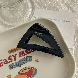 Detail view of a black cutout triangular hair claw clip on a creamy lifestyle tray