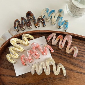 Set of wavy acetate hair claws in various marble and tortoiseshell patterns on wooden tray