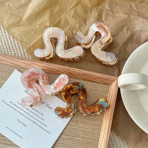 Elegant wave-shaped acetate hair claws in amber and pearl finishes on a wooden tray