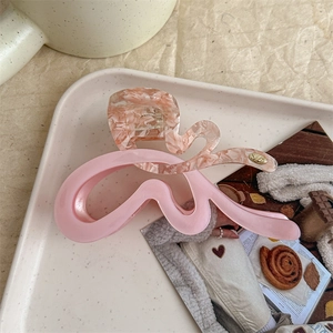 Detailed view of pink marble acetate wave hair claw with elegant gold logo on beige tray