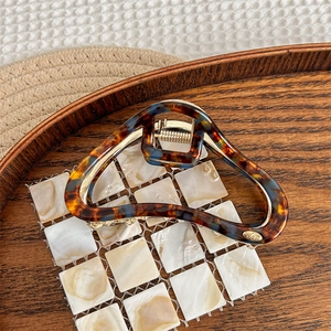 Detailed macro view of the tortoiseshell acetate hair claw with a small gold logo charm