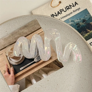 Detail of large wavy hair claw clip with pearlescent finish on a minimalist marble table