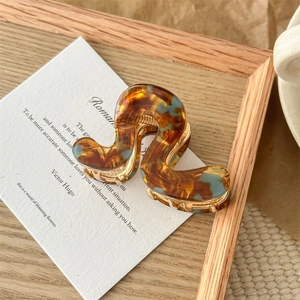 Detail view of wavy amber and blue acetate hair claw with gold metal spring mechanism