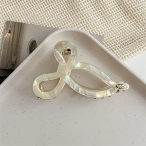 Detail of cream pearlescent hair claw clip with metallic YD logo on ceramic plate