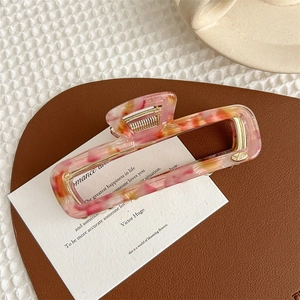 Detailed close-up of a pink marble acetate hair claw clip with golden metal spring