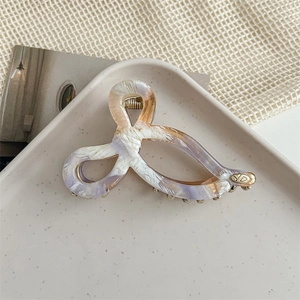 Detail of marbled acetate hair claw clip with golden metal spring and YD logo plaque