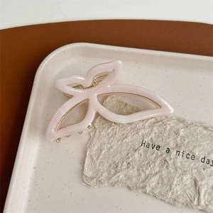 Detail of pink bow-shaped acetate hair claw clip with golden metal spring on a ceramic tray
