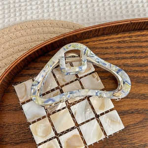 Detail of blue and beige marbled acetate hair claw clip with golden metal logo and spring