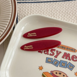 Dettaglio di due fermagli per capelli bordeaux con elegante scritta dorata Barrette LaFrance