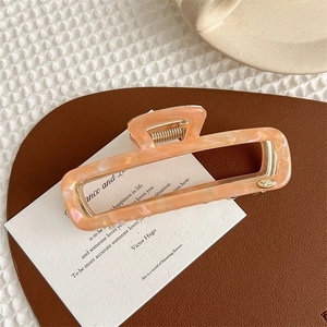 Detail of pink marble acetate hair claw clip with rectangular hollow design and gold spring