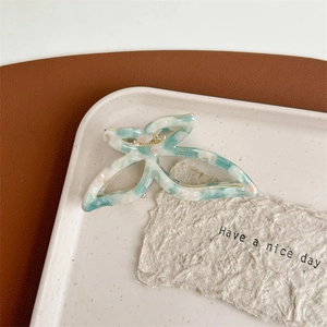 Detailed view of acetate bow hair claw clip with marble texture on ceramic tray