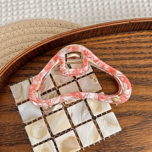 Detail of coral marble acetate hair claw with gold metal hinge and carved logo