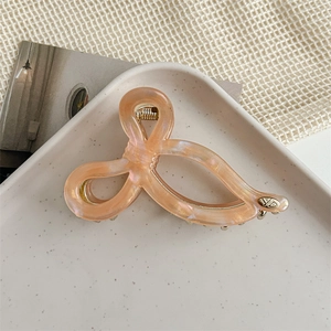 Macro detail of peach acetate hair claw clip featuring golden YD logo and marbled texture