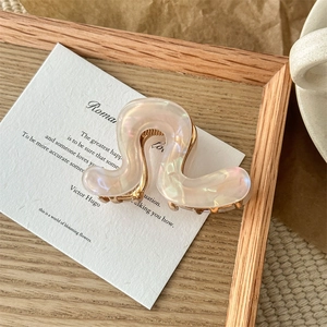 Macro detail of wave-shaped pearlescent resin hair claw with golden metal spring