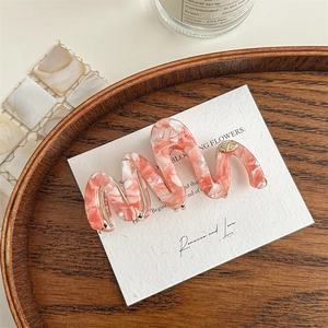 Detailed macro of pink and white acetate wavy hair claw with a gold metal XD logo