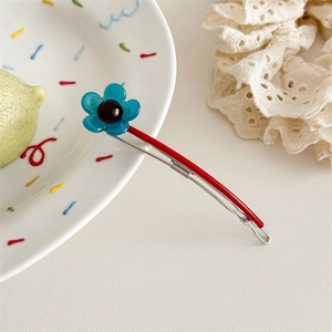 Detailansicht einer blauen Blumen-Haarklammer mit roter Metallbasis auf weißem Teller