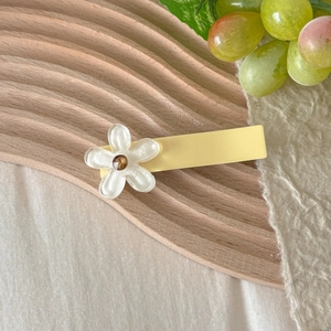 Close-up of yellow floral hair clip with white pearl finish flower on a wooden tray