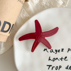Close-up of deep red starfish hair clip placed on a ceramic plate with lace background