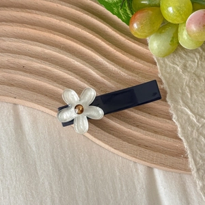 Detailed macro view of a blue flower hair clip with pearl white petals on wood