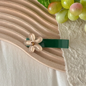 Detail of a dark green hair clip with a translucent pink flower and a yellow rhinestone