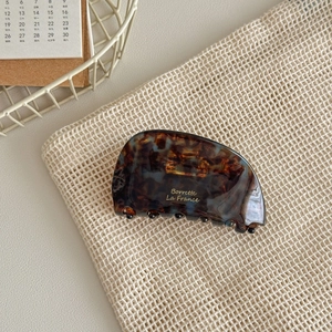 Macro view of vintage tortoiseshell hair claw clip with golden script logo on mesh bag
