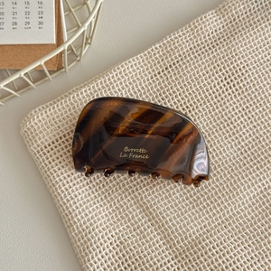 Detail of tortoise shell acetate hair claw clip with gold Borrette lettering on fabric