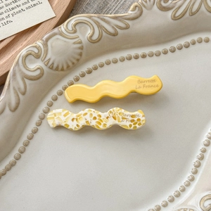 Detail of yellow and tortoiseshell acetate wave hair clips with gold lettering on a plate