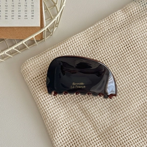 Detailed shot of dark brown acetate hair claw with gold logo on beige mesh fabric