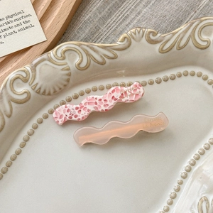 Detailed macro view of wavy acetate hair clips in pink texture on a ceramic tray