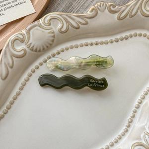 Detail of wavy acetate hair clips in olive green and marbled lake blue finish