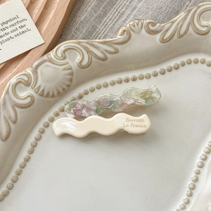 Macro detail of wavy acetate hair clips with Barrette La France text on a ceramic tray